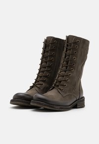 Botas de cuero verde oliva con cordones, punta redondeada, ojales de metal y una suela de goma texturizada. Cuentan con una cremallera lateral para un acceso fácil.