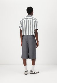 Short-sleeve, collared shirt with blue and white vertical stripes; paired with gray knee-length shorts. Model wears white socks and sneakers.
