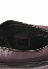 Innenansicht einer lila Ledertasche mit glatter Textur, schwarzer Innenauskleidung, Reißverschlussfach und einem Logo-Patch an der Seite.