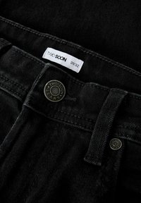 Černé džíny z denimu s kovovým knoflíkem se značkou "TWO SOON", bílá visačka s velikostí 31/32 a kontrastními švy.