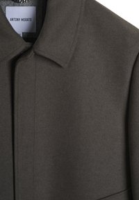 Donkergrijze jas van een zachte, gestructureerde stof. Voorzien van een standaard kraag, verborgen knoopsluiting en een label met "ANTONY MORATO."
