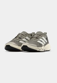 Γκρι αθλητικά παπούτσια με υφή στο πάνω μέρος, που διαθέτουν τρεις λευκές ρίγες, μαύρη καουτσούκ σόλα και διακοσμητικό στο τακούνι με σχέδιο.