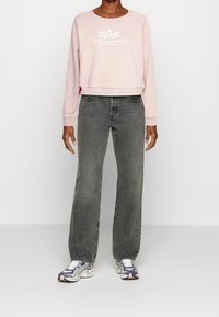 Světlounce růžová krátká mikina s bílým logem, doplněná o vysokým pasem tmavě šedé džíny s rovnými nohavicemi a sportovní barevné tenisky.