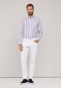 Chemise en coton rayée bleue, rouge et blanche, avec une poche poitrine et un col ; associée à un pantalon blanc et des baskets navy.