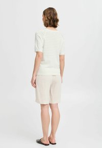 Lichte gebreide top met korte mouwen en een opengewerkt patroon, gecombineerd met beige linnen shorts. De look wordt afgerond met zwarte instappers.