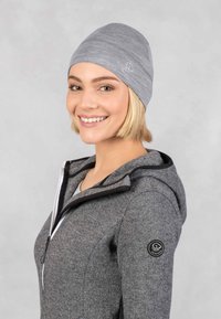 Bonnet gris avec une texture serrée et lisse, arborant un logo discret sur le côté. Porté avec un sweat à capuche zippé gris. Design doux et décontracté.