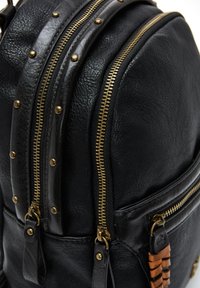Mochila de cuero negro con tres compartimentos con cremallera dorada, remaches y un acento de cuero trenzado en el lateral. Superficie texturizada.
