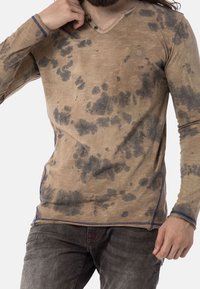 T-shirt beige a maniche lunghe con un motivo grigio marmorizzato, scollo a V e accenti di cucitura blu lungo le cuciture. Tessuto morbido.