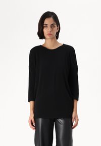Fekete oversized pulóver kerek nyakkivágással és háromnegyedes ujjal, puha anyagból készült. Fekete műbőr nadrággal párosítva.