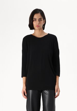 Black oversized sweater with a round neckline and three-quarter sleeves, made from a soft fabric. Paired with black faux leather pants.