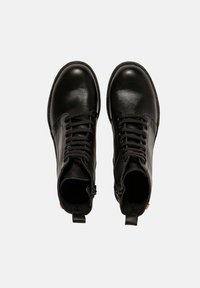 Par de botines de cuero negro con cordones, cremallera lateral, puntera redondeada y tiradores en la parte posterior, mostrados desde una vista superior sobre fondo blanco.