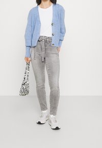 Cárdigan de punto azul claro con escote en V, tres botones, combinado con unos pantalones vaqueros grises de talle alto y un bolso de estampado de cebra en blanco y negro.