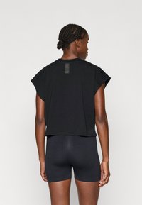 Schwarzes, kurzärmliges Oberteil mit Rundhalsausschnitt, strukturiertem Rückenteil und lässiger Passform, kombiniert mit schwarzen, figurbetonten Shorts.