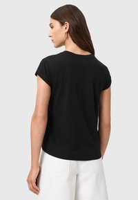 Camiseta negra de cuello redondo con mangas cortas enrolladas, hecha de una tela suave, que presenta un ajuste relajado y una textura lisa.