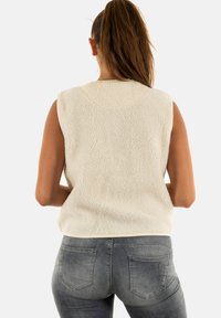Gilet en polaire crème avec une surface texturée, design sans manches et encolure arrondie, associé à un jean gris ajusté avec des détails de couture subtils.