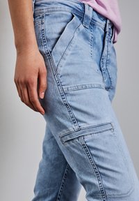 Ljusblå denim-cargobyxor med sidofickor, synlig sömnad och en något blekt struktur. Tight passform med medelhög midja.