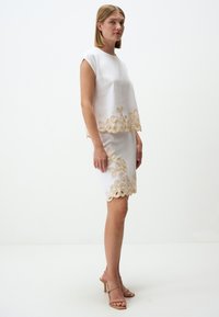 Completo bianco composto da un top e una gonna, con ricami floreali dorati sui bordi. Tessuto liscio, maniche corte e design aderente.