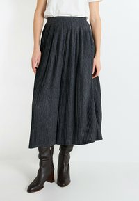 Falda midi plisada de color gris oscuro hecha de tejido texturizado, combinada con botas de cuero marrón hasta la rodilla con tacón cuadrado.