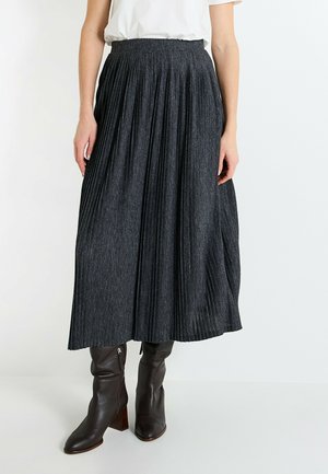Falda midi plisada de color gris oscuro hecha de tejido texturizado, combinada con botas de cuero marrón hasta la rodilla con tacón cuadrado.