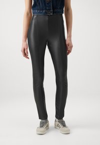 Zwarte faux leren skinny spijkerbroek met een gladde textuur en verticale naden, gecombineerd met een spijkerjas en grijze sneakers.