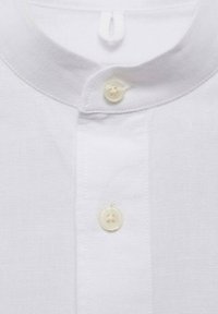 Chemise en lin blanc avec un col mao et deux petits boutons blancs visibles fermés le long de la patte de boutonnage.