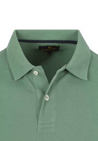 Polo shirt in zacht groen, met een gemêleerde stof, gevouwen kraag, een biologische knoopsluiting met twee knopen en een binnenste marineblauwe afwerking. Merketiket zichtbaar aan de binnenkant.