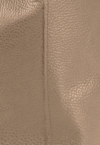 Getextureerd lichtbruin leer met een subtiel nerfpatroon, voorzien van een zichtbare naad, wat duidt op soepel en duurzaam materiaal.