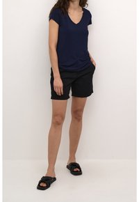 Camiseta de cuello en v azul marino de manga corta, combinada con pantalones cortos negros y sandalias negras con un diseño de nudo.