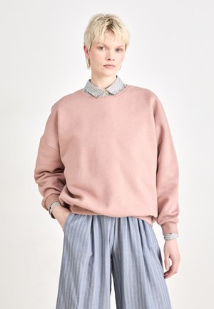 Felpa rosa chiaro con vestibilità ampia e scollo a girocollo, abbinata a pantaloni a gamba larga a righe blu e una camicia con colletto sotto.