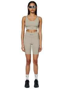 Khaki sportowy stanik i dopasowane szorty rowerowe z logo 'HALO'. Gładki, elastyczny materiał; model nosi czarne sneakersy i białe skarpetki.