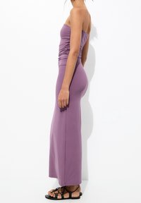 Robe violette sans bretelles avec un corsage fronc é, jupe longue et fluide, et une texture lisse. Associée à des sandales plates noires.