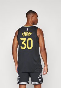 Sort basketballtrøje med "CURRY" og nummer "30" i gul. Har rund halsudskæring og blå detaljer. Stoffet ser åndbart ud.