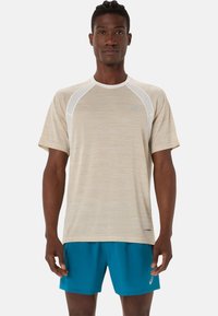 T-shirt de sport beige clair en tissu texturé, avec des manches raglan et des accents blancs ; associé à un short bleu, mettant en avant un design sportif.