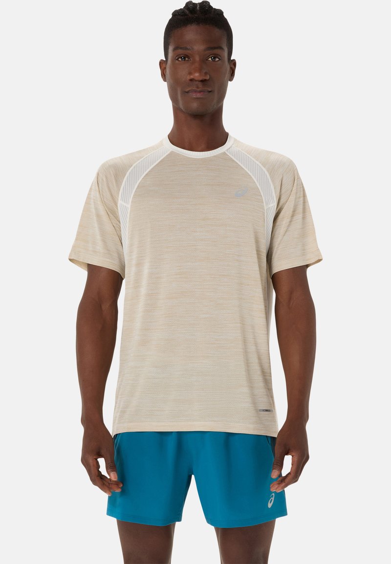 T-shirt de sport beige clair en tissu texturé, avec des manches raglan et des accents blancs ; associé à un short bleu, mettant en avant un design sportif.