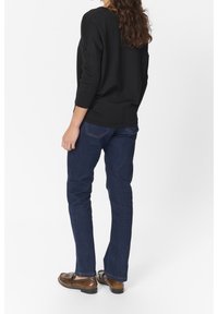 Pull noir côtelé avec manches trois-quarts, associé à un jean droit bleu foncé et des chaussures en cuir marron. Vue de dos sans accents notables.