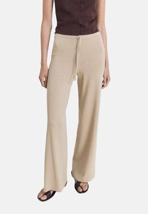 Beige wijde broek gemaakt van zachte stof, met een trekkoord in de taille. Gepaard met een donkere knooptop en platte zwarte sandalen.