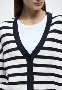 Marineblå og hvitstripet cardigan med V-hals, med to svarte knapper foran og en lyseblå t-skjorte under.