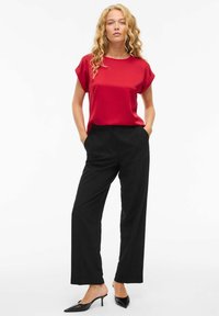 Top corto in satin rosso a maniche corte abbinato a pantaloni larghi neri. Il modello indossa tacchi a punta neri. Design semplice e pulito.
