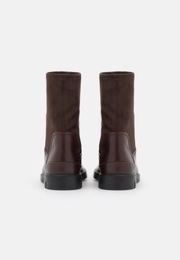 Bottines en daim marron avec des accents en cuir bordeaux brillant et une semelle en caoutchouc noir texturée, dotées d'un bout rond et de coutures lisses.