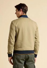 Felpa color khaki con colletto blu e polsini a costine. Presenta una texture liscia e una vita elasticizzata per un look aderente.