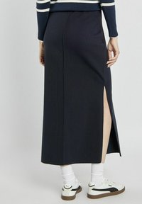 Granatowa maxi spódnica z bocznym rozcięciem i gładkim, dopasowanym krojem. W połączeniu z białymi trampkami, ukazującymi skarpetki do kostek.