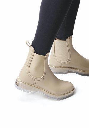 Botas Chelsea de goma beige con paneles elásticos en los laterales, suelas transparentes y detalles de costura. Adecuadas para condiciones húmedas y uso informal.