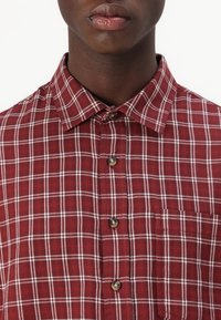 Rotes Karomusterhemd mit Button-Down-Kragen, weißem Karomuster und einer einzelnen Brusttasche. Hergestellt aus strukturiertem Stoff mit lässiger Passform.