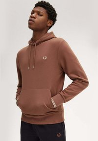 Felpa marrone con cappuccio e cordini, tasca a marsupio e polsini a costine. Presenta un piccolo logo ricamato sul petto. Tessuto morbido al tatto.