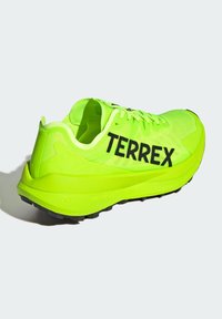Scarpa da corsa verde lime con tomaia in rete, ammortizzazione spessa e logo "TERREX" nero. Presenta una suola testurizzata per una migliore aderenza.