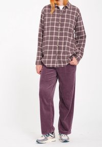 Chemise à carreaux boutonnée dans des tons violet pâle avec des lignes grises et blanches, associée à un pantalon large en velours côtelé d'un violet profond. Chaussures de sport présentées.