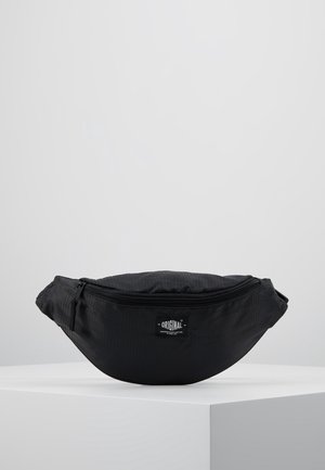 Sort stoftalje taske med lynlås foran og "Original" mærkat, vist på en hvid platform mod en grå baggrund.