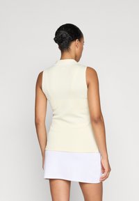 Camisola polo sem mangas e colarinho em tecido canelado amarelo pálido. Combinada com uma saia branca, exibindo um design minimalista e desportivo.