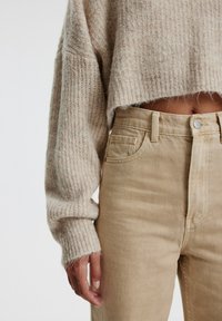 Beige ribbeltrui met lange mouwen, cropped zoom, gecombineerd met hooggetailleerde beige corduroy broek met subtiele voorkwartjes en knoopsluiting.