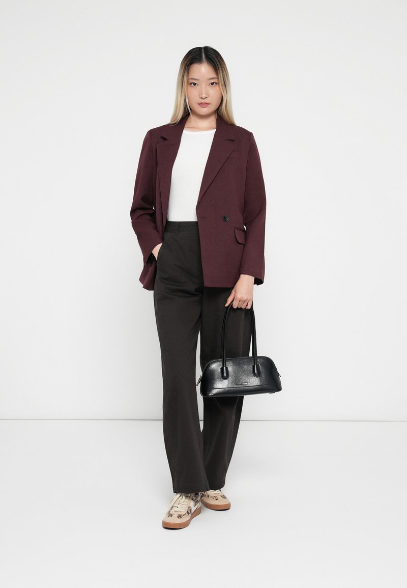 Blazer personalizzato color bordeaux, top bianco, pantaloni neri a gamba larga, borsa nera testurizzata e sneakers beige con accenti a motivo.